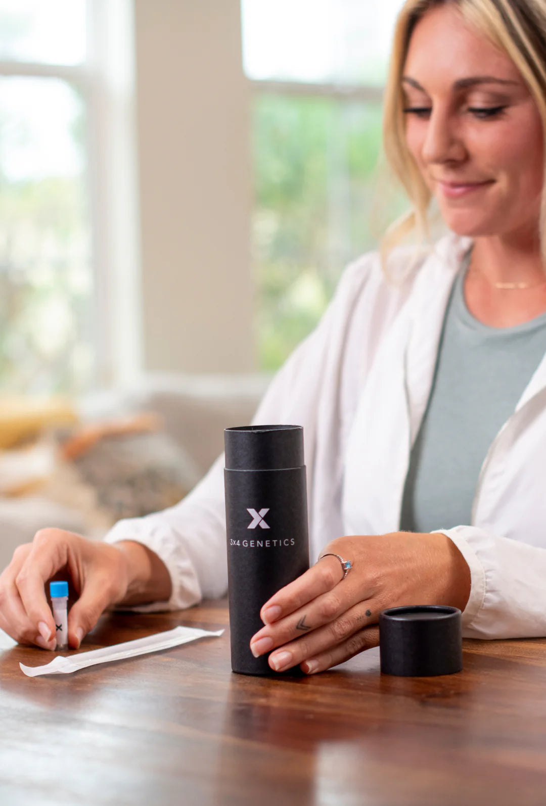 Black cylindrical bottle with X logo on table next to writing hands